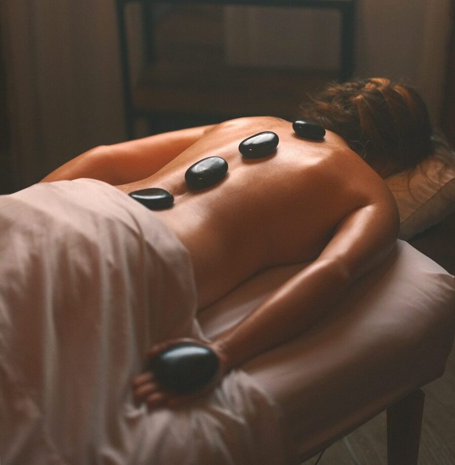 a woman laying on a bed with hot stones on her back